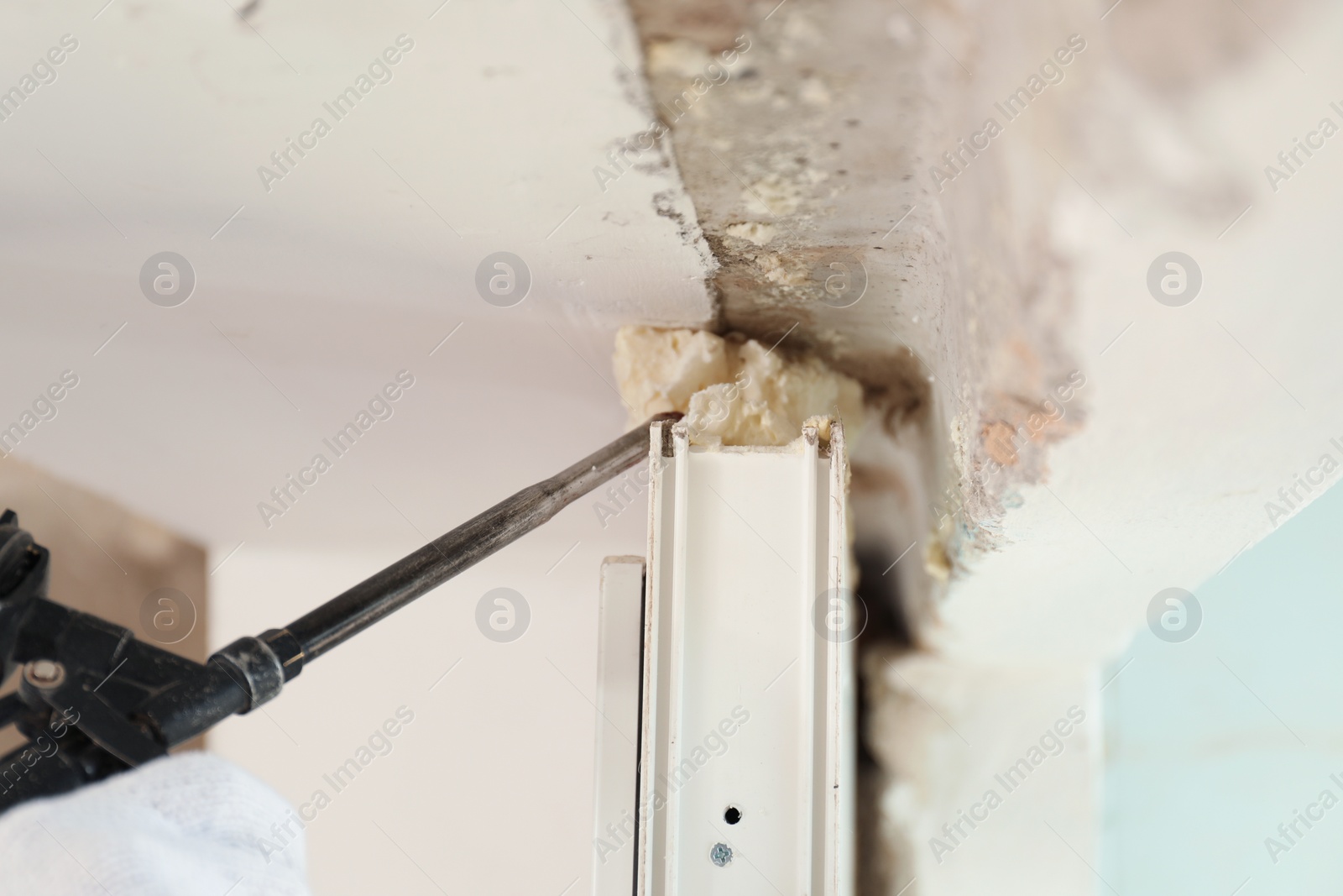 Photo of Worker using foam gun for window installation indoors, closeup