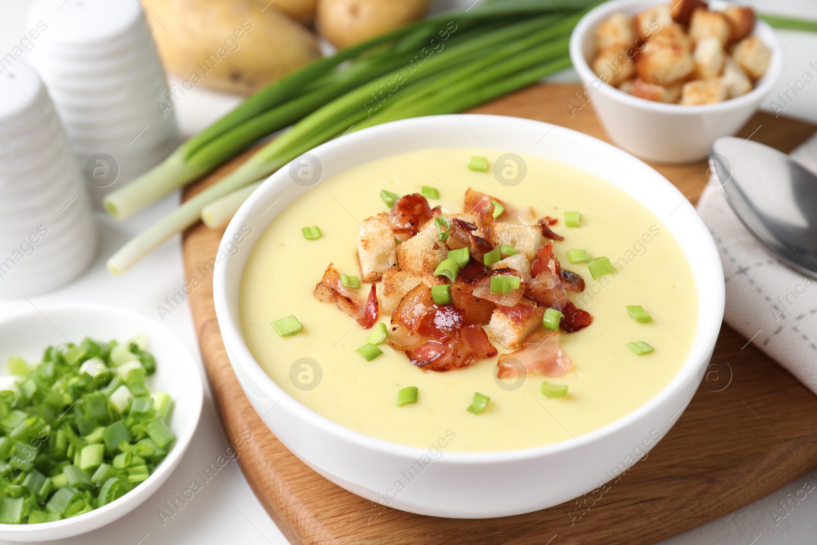 Photo of Tasty potato soup with bacon, green onion and croutons in bowl served on white table