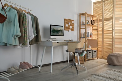 Photo of Stylish room interior with comfortable workplace and rack of clothes