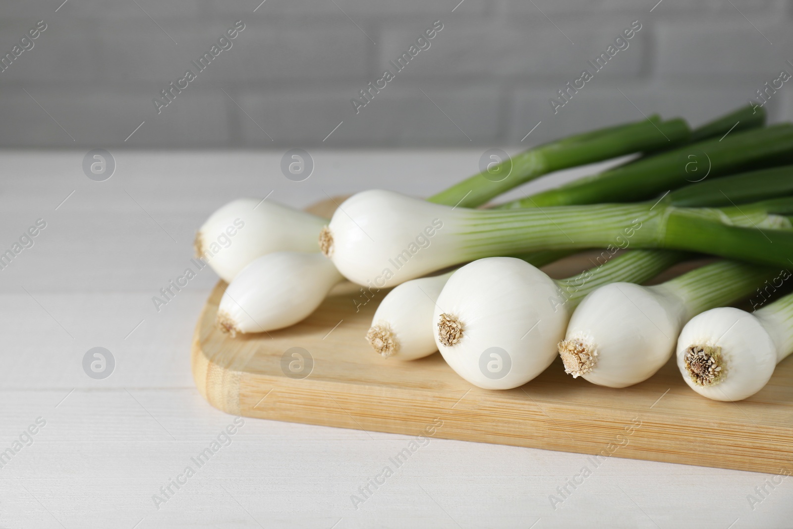 Photo of Fresh green spring onions on white wooden table, closeup. Space for text