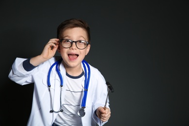 Cute little child in doctor uniform with reflex hammer on black background. Space for text