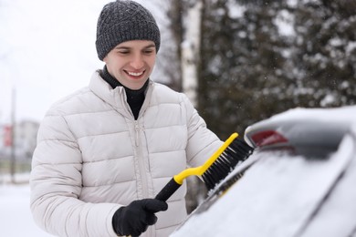 Man cleaning snow from car window outdoors