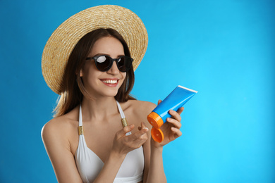 Young woman applying sun protection cream on light blue background