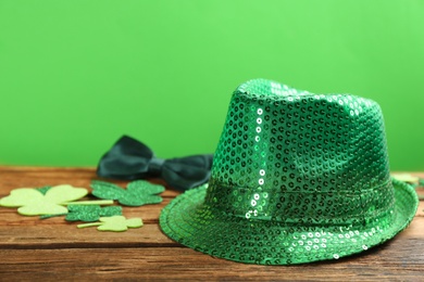 Photo of Green sequin hat, decorative clover leaves and bow tie on wooden table against green background, space for text. St Patrick's Day celebration