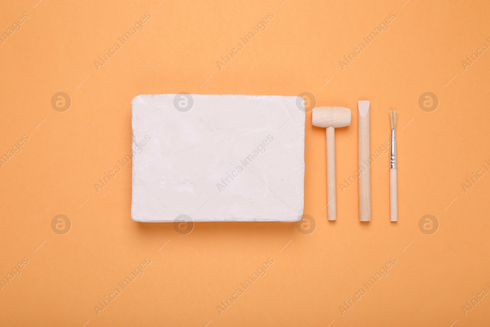 Photo of Educational toy for motor skills development. Excavation kit (plaster, digging tools and brush) on orange background, flat lay