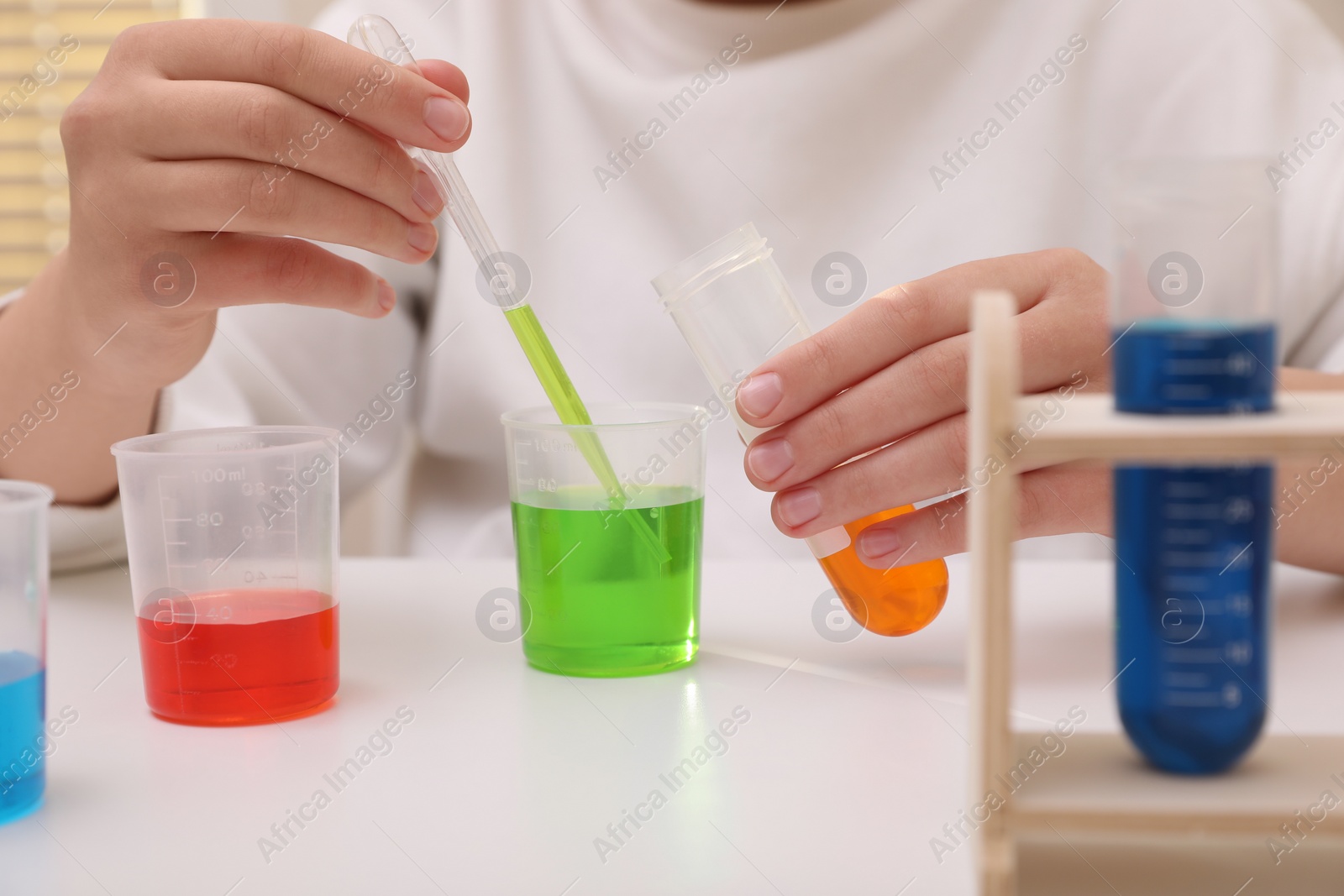 Photo of Girl mixing colorful liquids at white table indoors, closeup. Chemical experiment set for kids