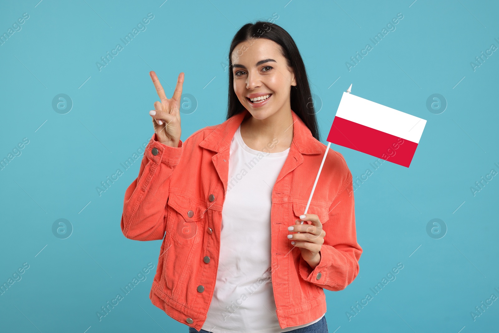 Image of Happy young woman with flag of Poland showing V-sign on light blue background