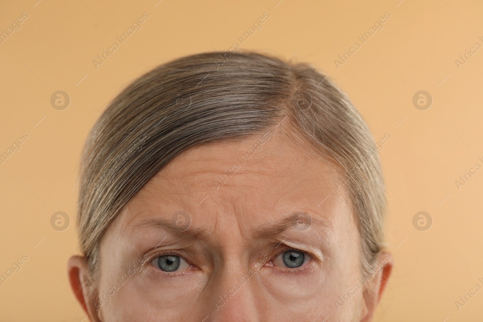 Photo of Woman with wrinkles on her forehead against beige background, macro view