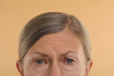 Woman with wrinkles on her forehead against beige background, macro view