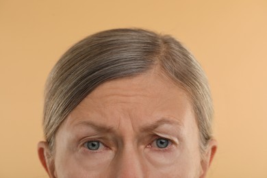 Photo of Woman with wrinkles on her forehead against beige background, macro view