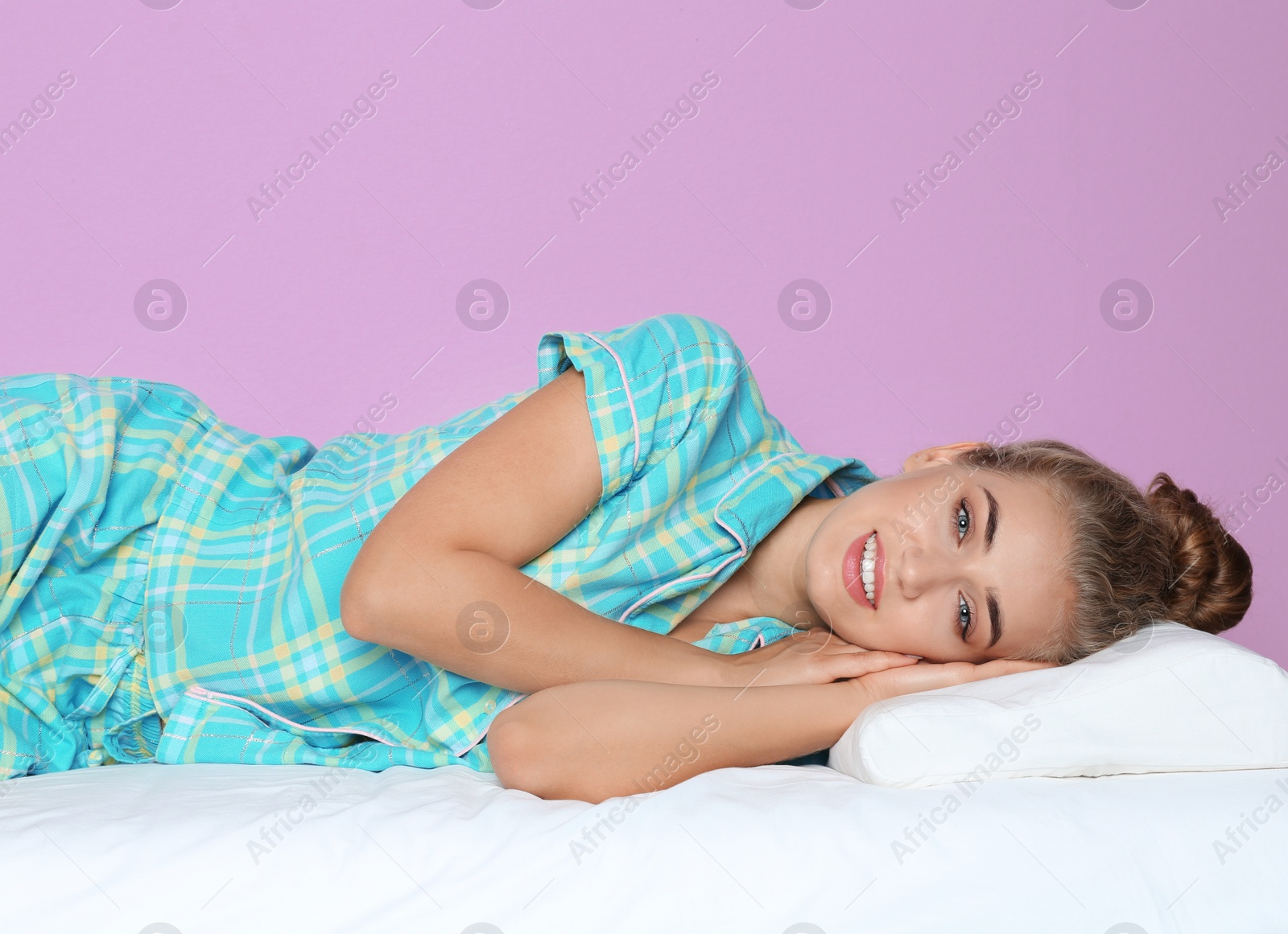 Photo of Beautiful woman lying with orthopedic pillow on bed against color background