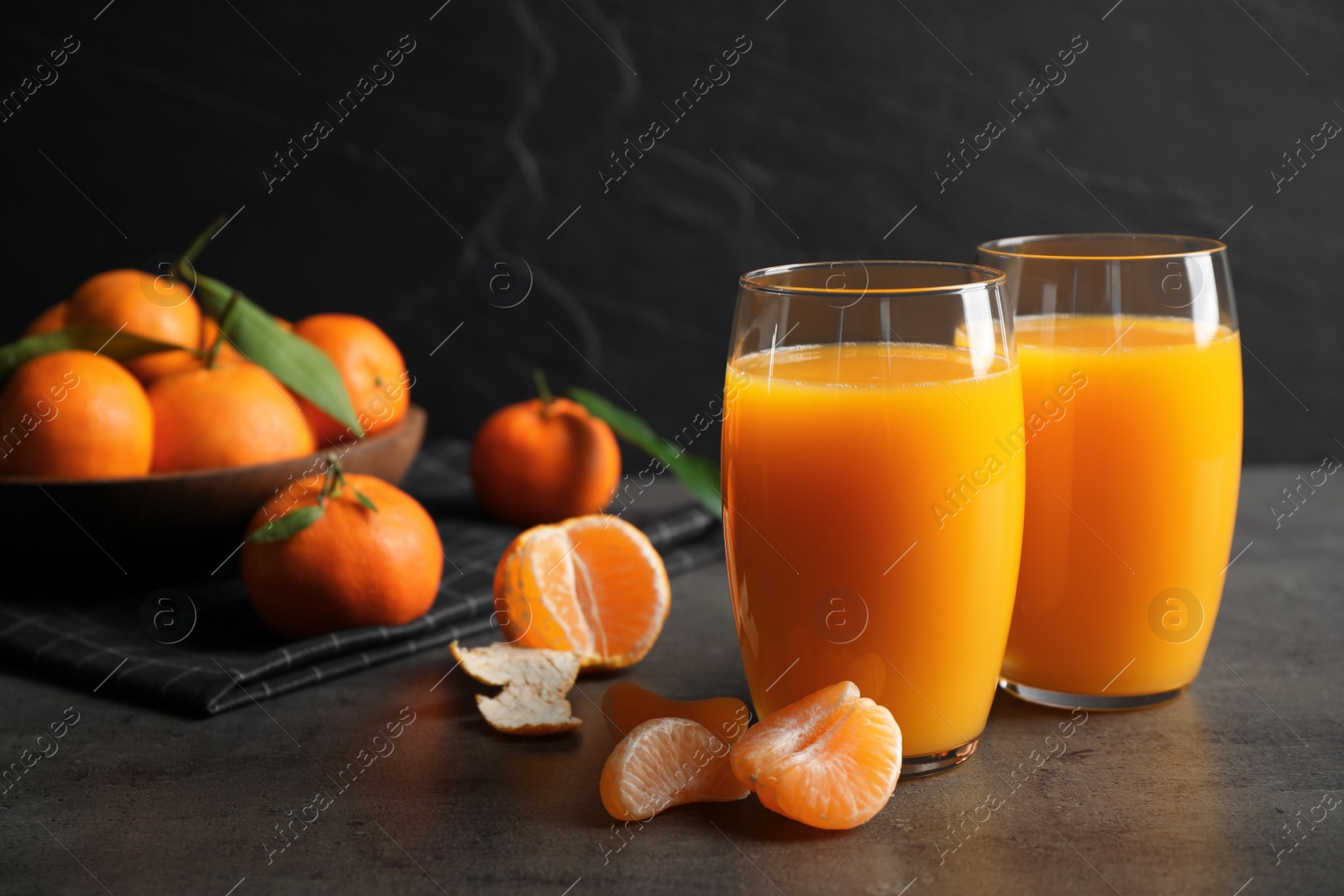 Photo of Fresh tangerines and glasses of juice on grey table