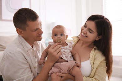 Photo of Happy couple holding their cute little baby with pacifier at home