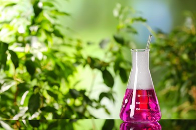 Laboratory flask with colorful liquid on glass table outdoors, space for text. Chemical reaction