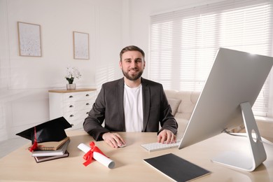 Photo of Happy student with graduation hat and diploma at workplace in office