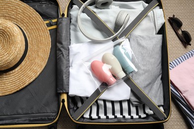 Photo of Plastic bag of cosmetic travel kit and clothes in suitcase, top view