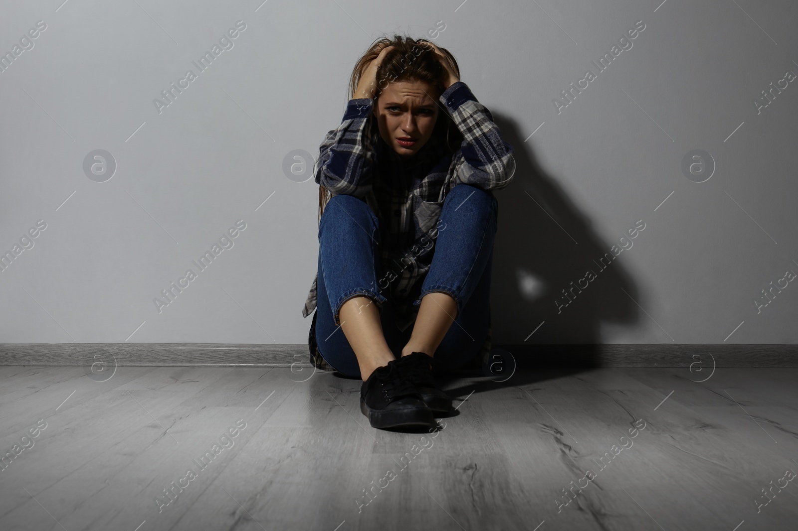 Photo of Abused young woman crying near white wall. Domestic violence concept