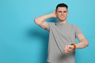 Photo of Emotional young man checking time on light blue background, space for text. Being late concept