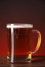 Mug with fresh beer on wooden table against color background, closeup