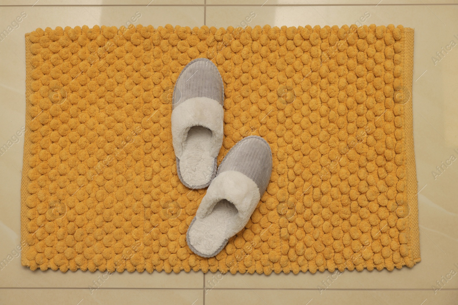 Photo of Soft orange bath mat and slippers on floor, top view