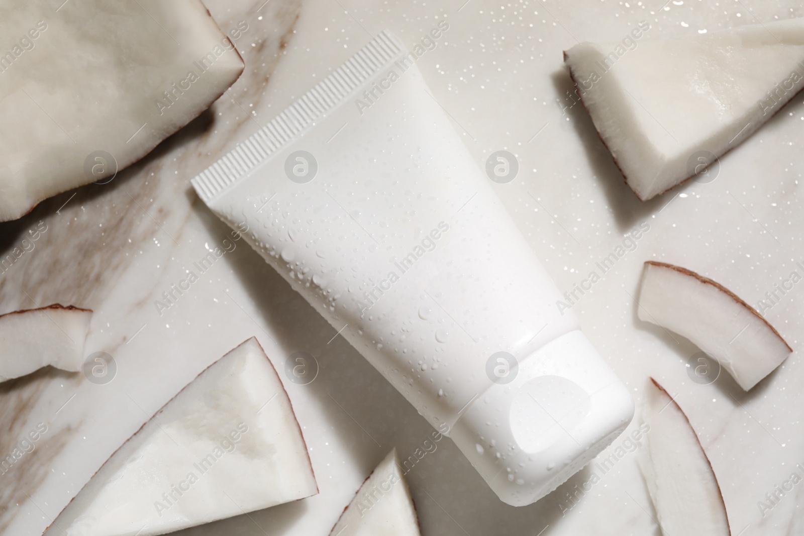 Photo of Tube of hand cream and coconut pieces on wet marble table, flat lay