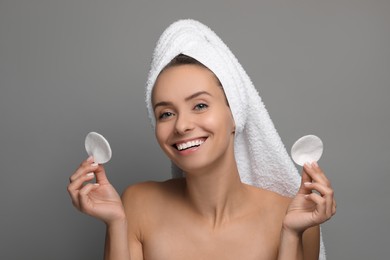 Photo of Smiling woman removing makeup with cotton pads on grey background