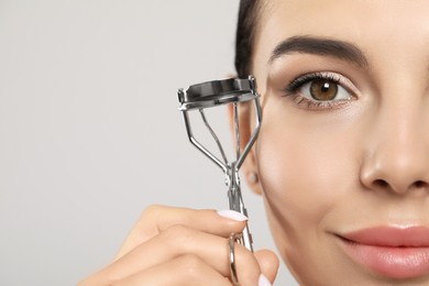 Photo of Beautiful young woman with eyelash curler on light grey background, closeup. Space for text