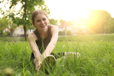 Teenage girl doing morning exercise on green grass in park, space for text