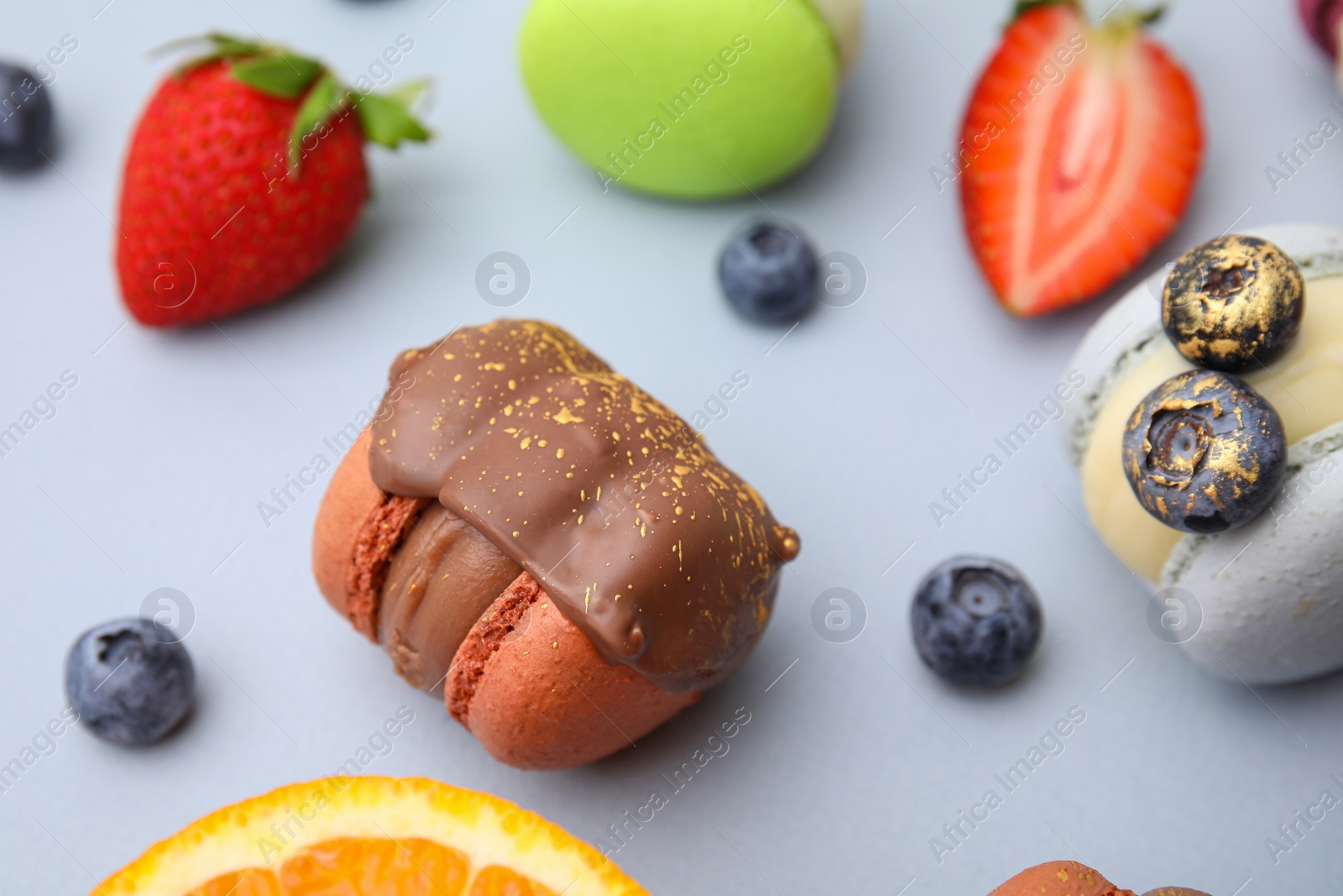 Photo of Delicious macarons, fruits and berries on light blue table, closeup