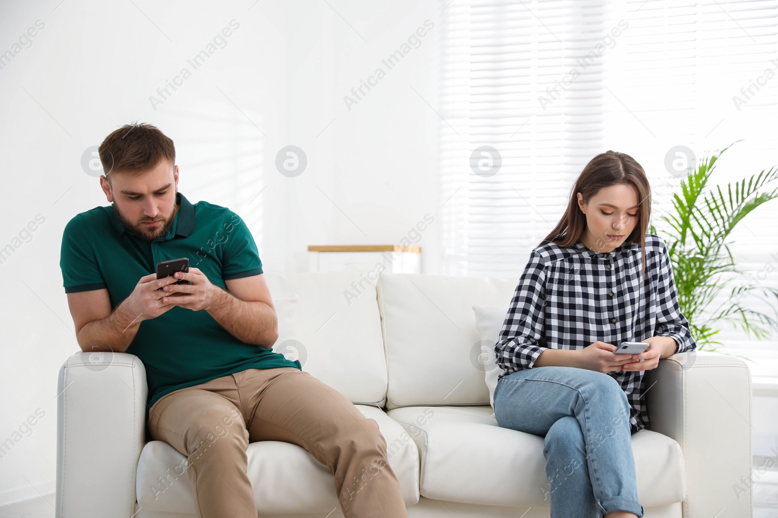 Photo of Couple addicted to smartphones ignoring each other at home. Relationship problems