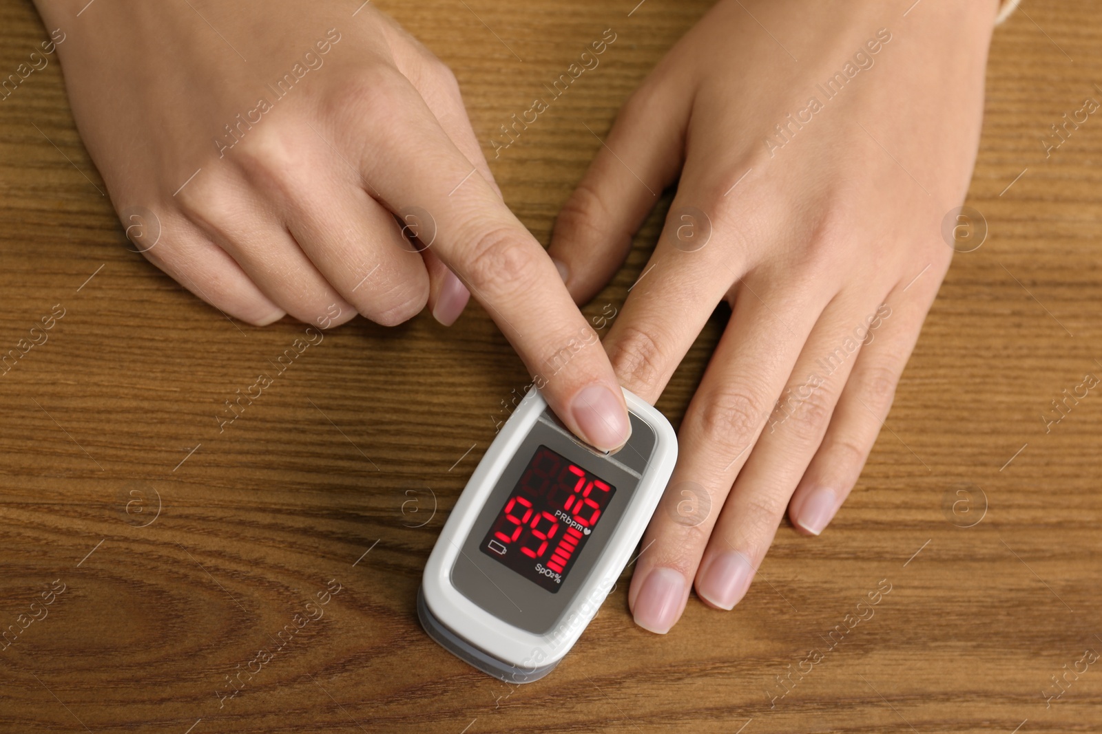 Photo of Woman using pulse oximeter for oxygen level testing at wooden table, above view