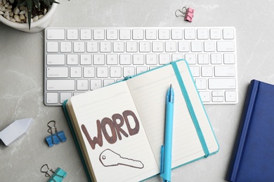 Notebook with drawn key, keyboard and stationery on light grey table, flat lay. Keyword concept