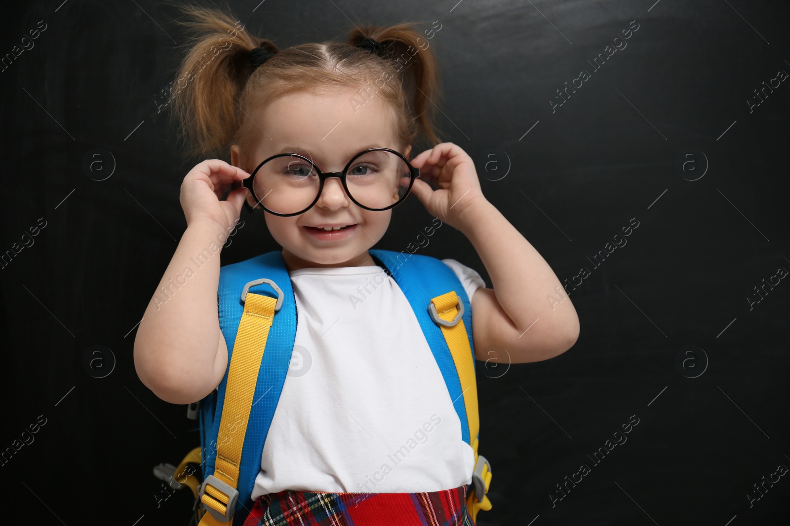 Photo of Cute little child wearing glasses near chalkboard. First time at school