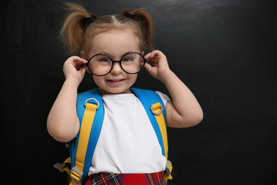 Photo of Cute little child wearing glasses near chalkboard. First time at school