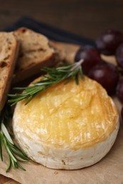 Photo of Tasty baked camembert, pieces of bread, grapes and rosemary on table, closeup
