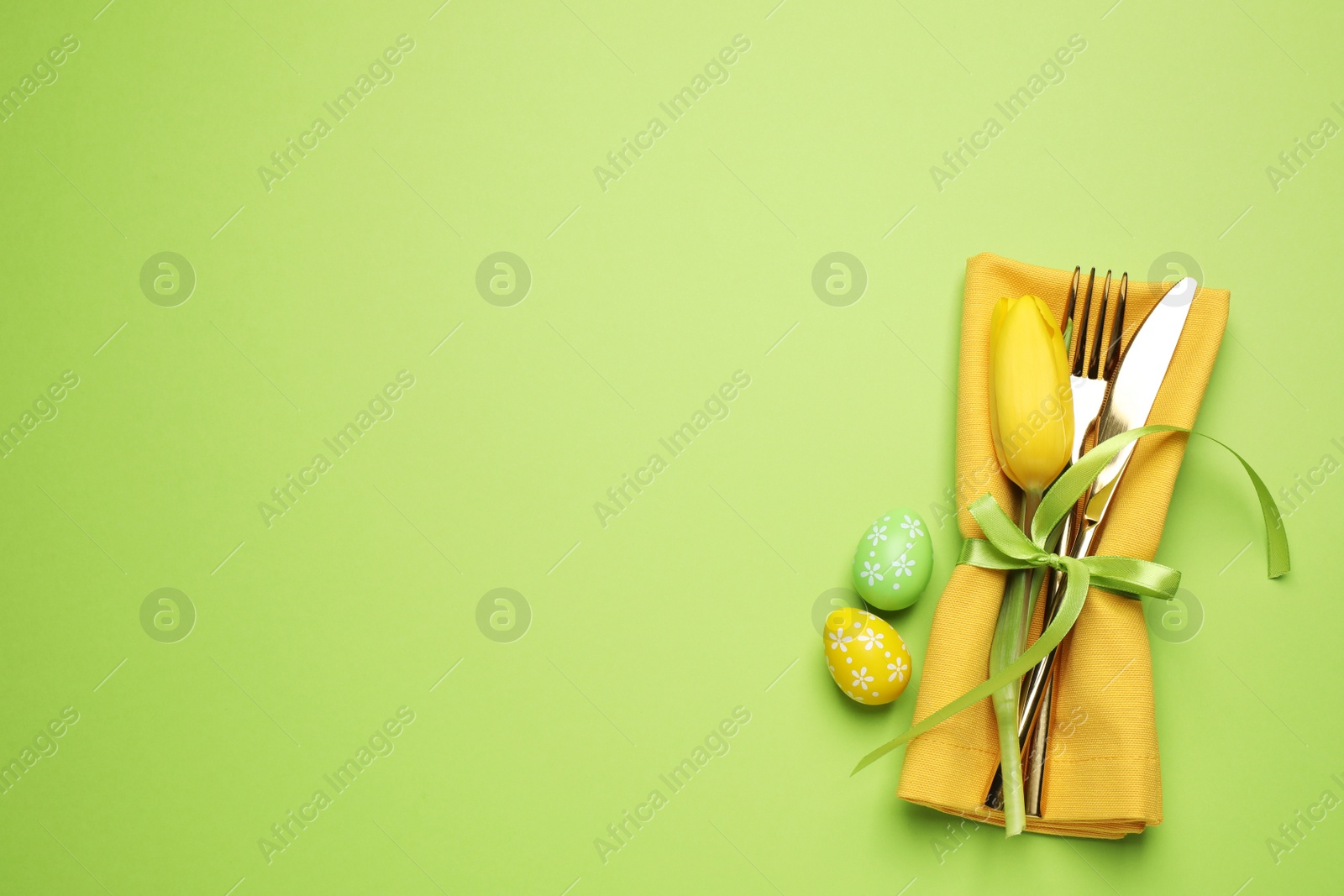 Photo of Top view of cutlery set with floral decor on green background, space for text. Easter celebration