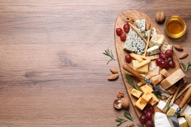 Photo of Cheese plate with honey, grapes and nuts on wooden table, flat lay. Space for text