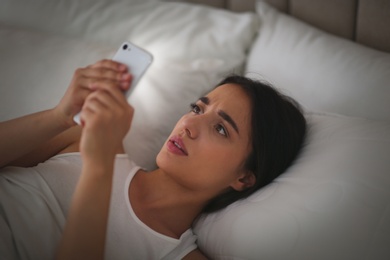 Photo of Emotional young woman with nomophobia using smartphone in bed at night. Insomnia concept