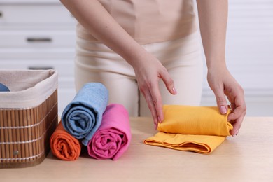 Photo of Woman rolling shirt at table in room, closeup. Organizing clothes