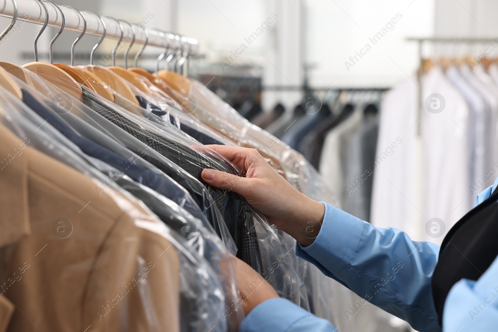 Photo of Dry-cleaning service. Woman taking jacket in plastic bag from rack indoors, closeup