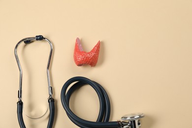 Photo of Endocrinology. Stethoscope and model of thyroid gland on beige background, top view. Space for text