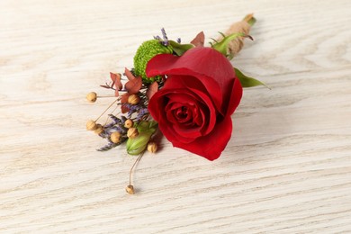 Stylish boutonniere with red rose on light wooden table, closeup