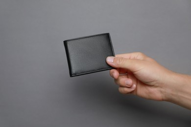 Photo of Man holding black leather wallet on dark grey background, closeup. Space for text