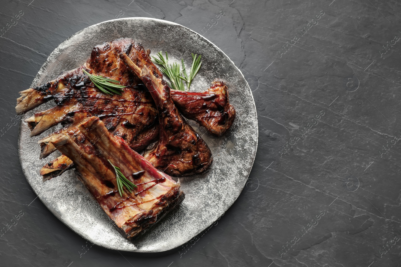 Photo of Delicious grilled ribs served on black table, top view. Space for text