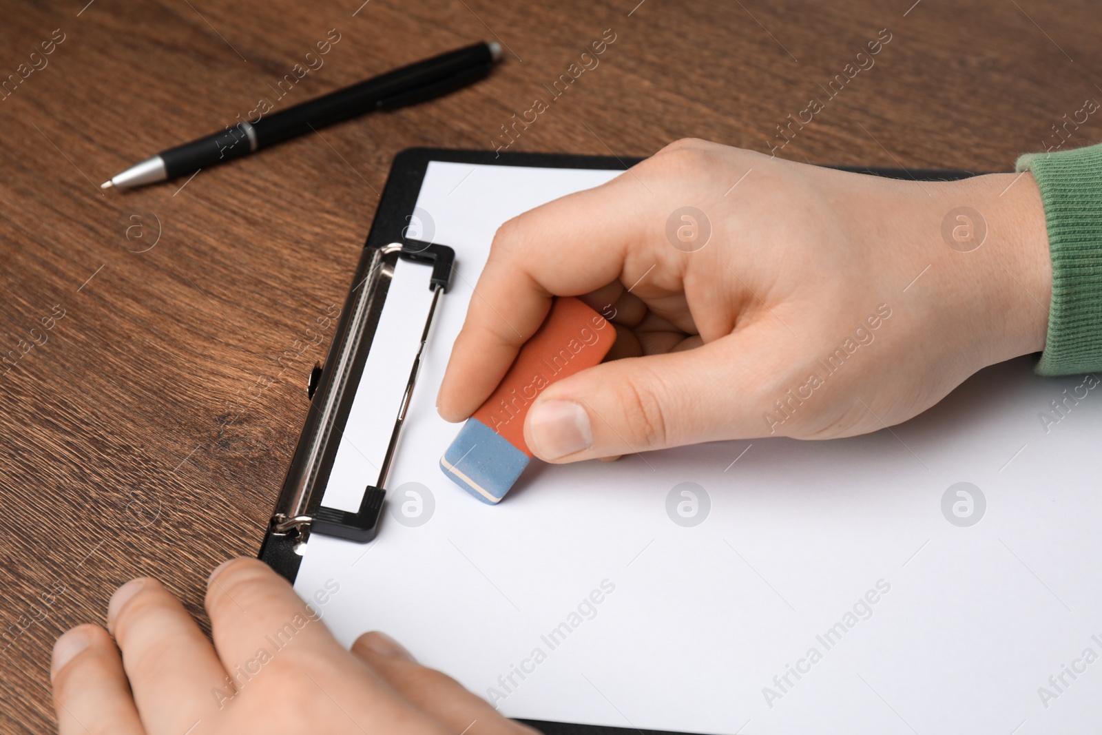 Photo of Man erasing something on paper at wooden table, closeup