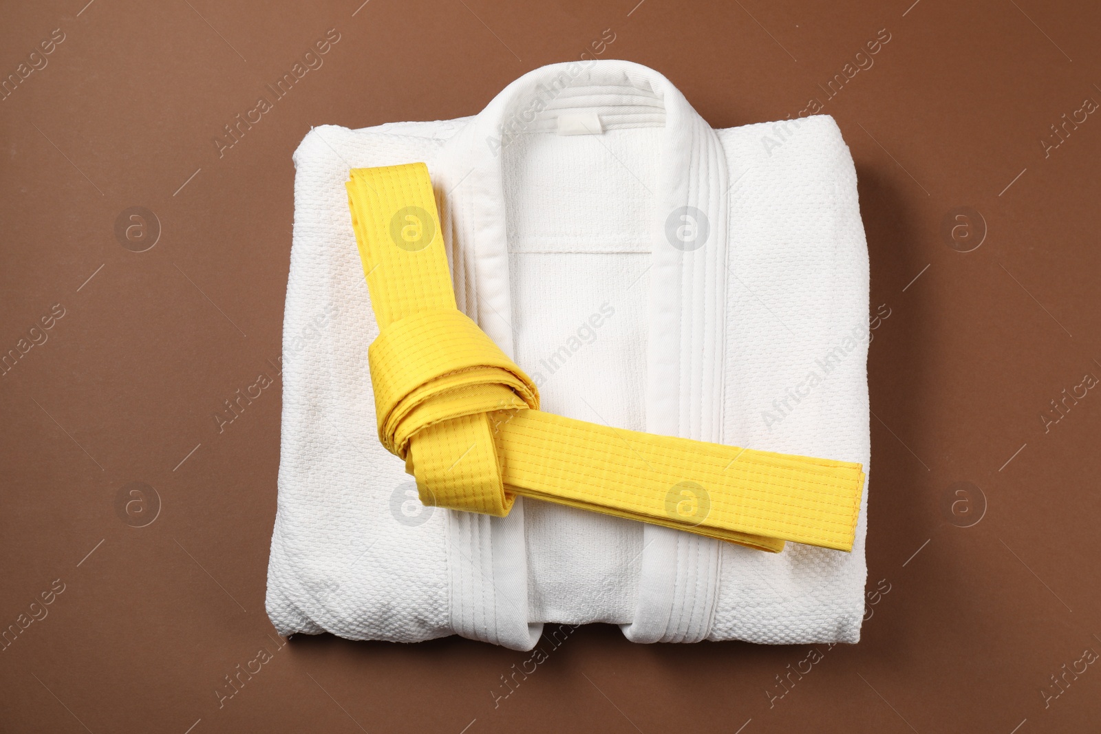 Photo of Yellow karate belt and white kimono on brown background, top view