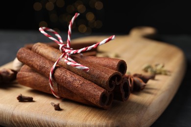 Cinnamon sticks and other spices on table against black background with blurred lights, closeup