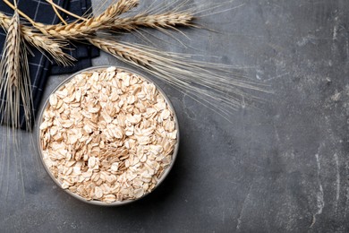 Photo of Bowl of oatmeal and spikelets on grey table, flat lay. Space for text