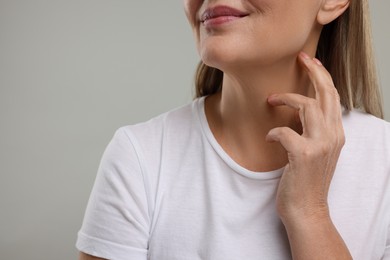 Photo of Mature woman touching her neck on grey background, closeup. Space for text