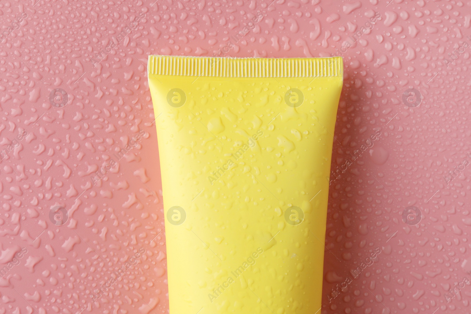 Photo of Moisturizing cream in tube on pink background with water drops, top view